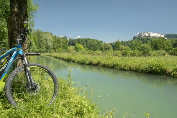 Sicht auf Burg Salzburg im Vordergrund ein Fluss und E Bike