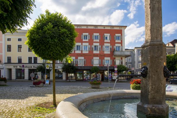 Der Brunnen der Mariensäule im Vordergrund mit historischen Gebäuden im Inn-Salzach-Stil am Marienplatz