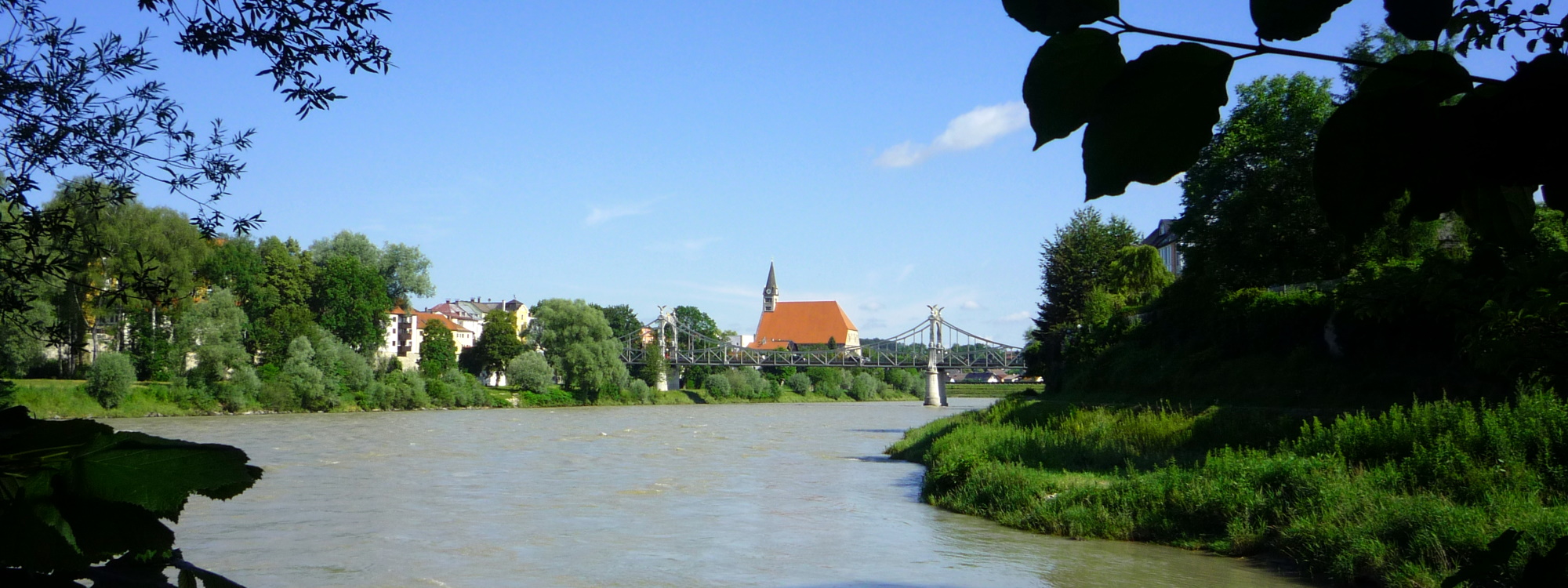 Landschaftsaufnahme des Salzachflussbetts mit Stiftskirche und Länderbrücke in der Ferne